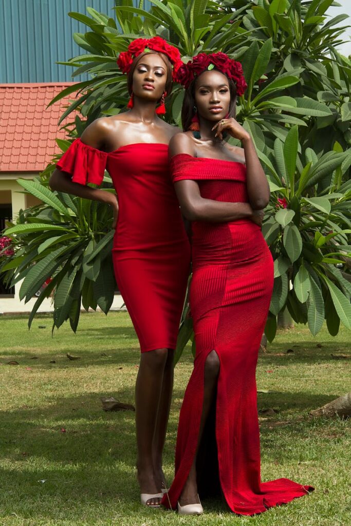 Two stylish women in red dresses and flower crowns posing outdoors.