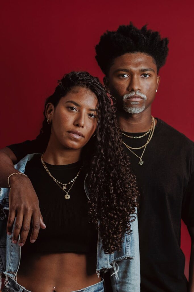 Fashionable couple posing together in a studio with a vibrant red background.