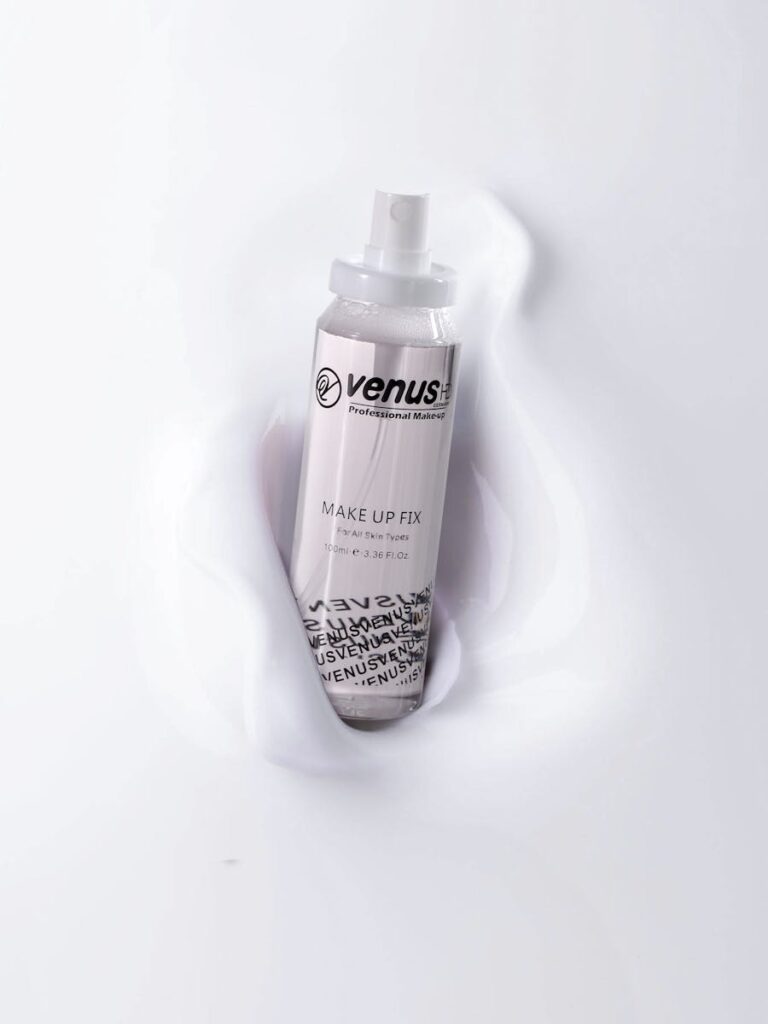 A sleek makeup fix spray bottle by Venus rests on a smooth white surface.