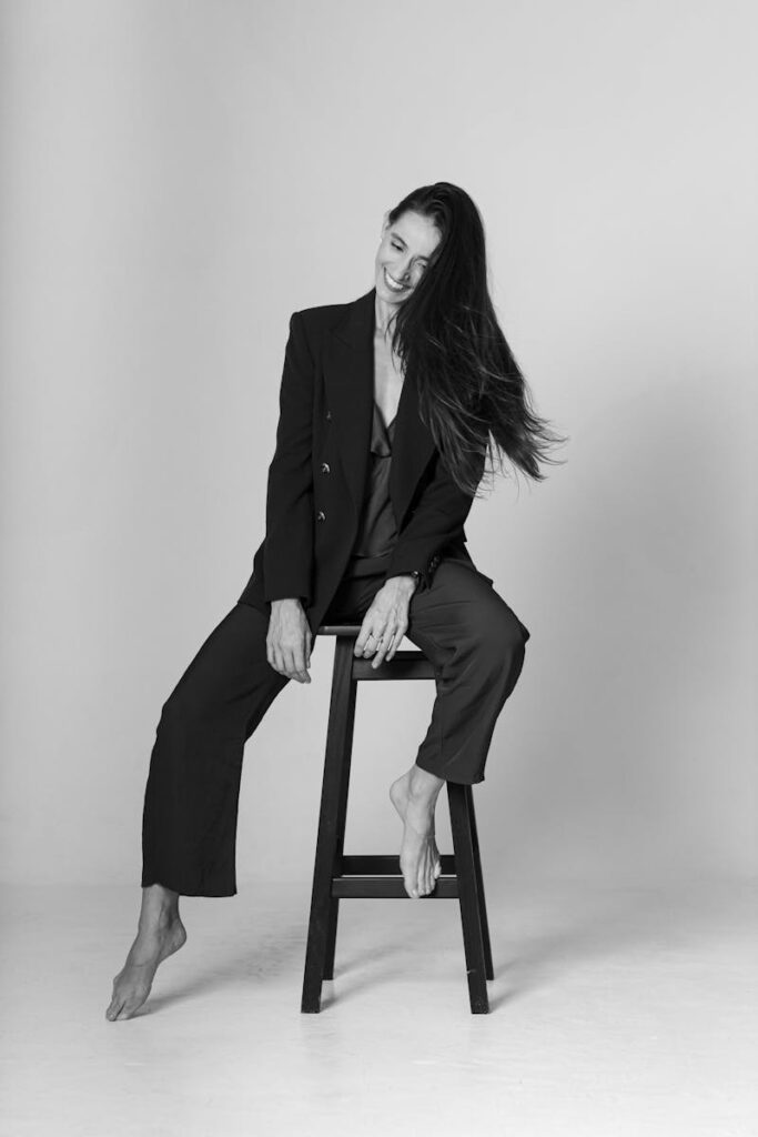 Black and white portrait of a woman in a suit sitting barefoot on a stool.