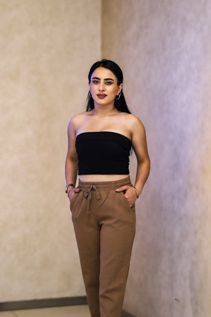 Young woman in black crop top and brown sweatpants posing indoors.