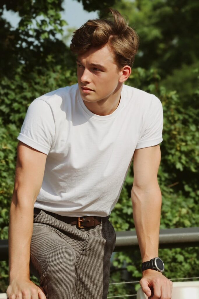 Fashionable young adult man posing confidently in a white t-shirt in Berlin park.