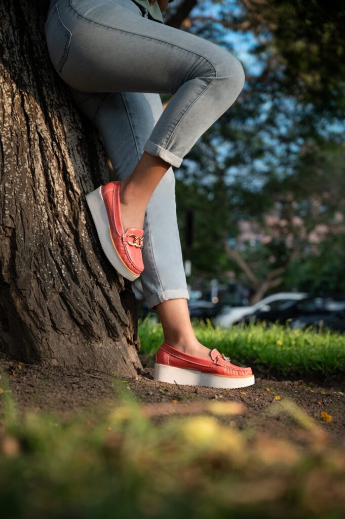 Legs of a woman in trendy jeans and shoes leaning against a tree on a sunny day.