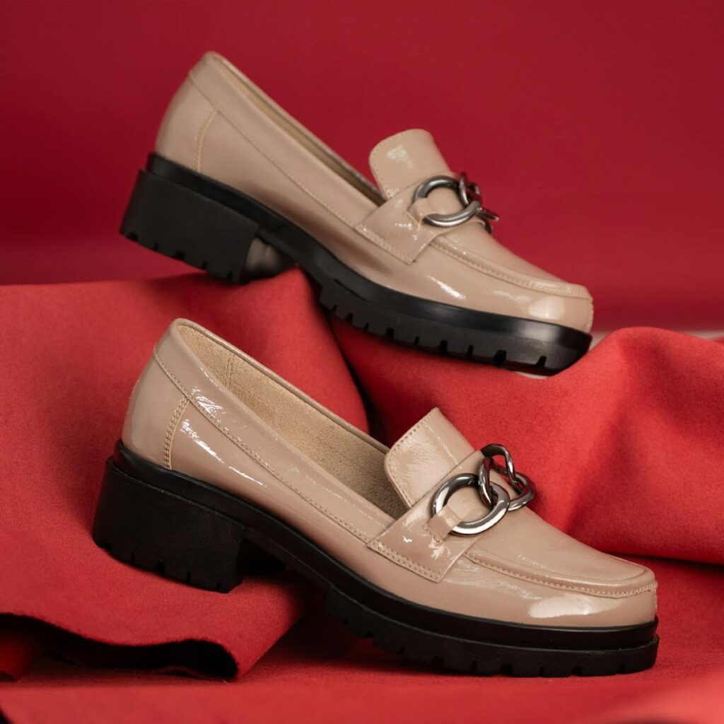 Stylish beige loafers with metallic detail showcased elegantly against a bold red backdrop, highlighting contemporary footwear design.