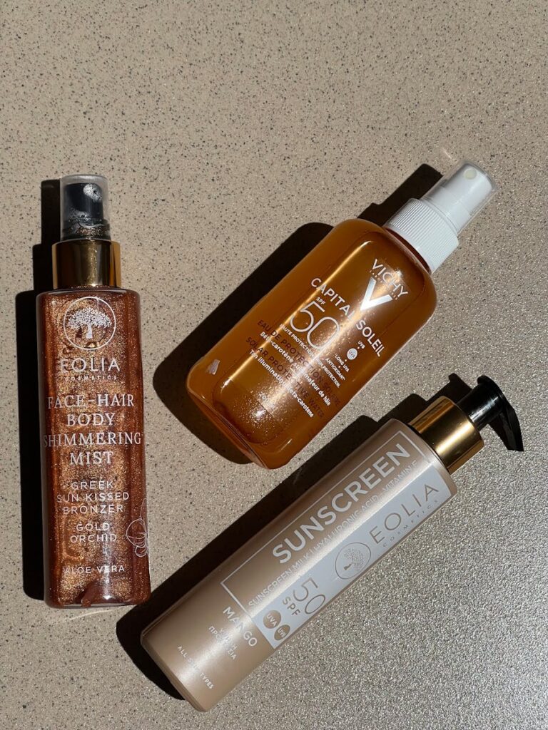 Flat lay of cosmetic bottles featuring sunscreen and body mist on textured surface.