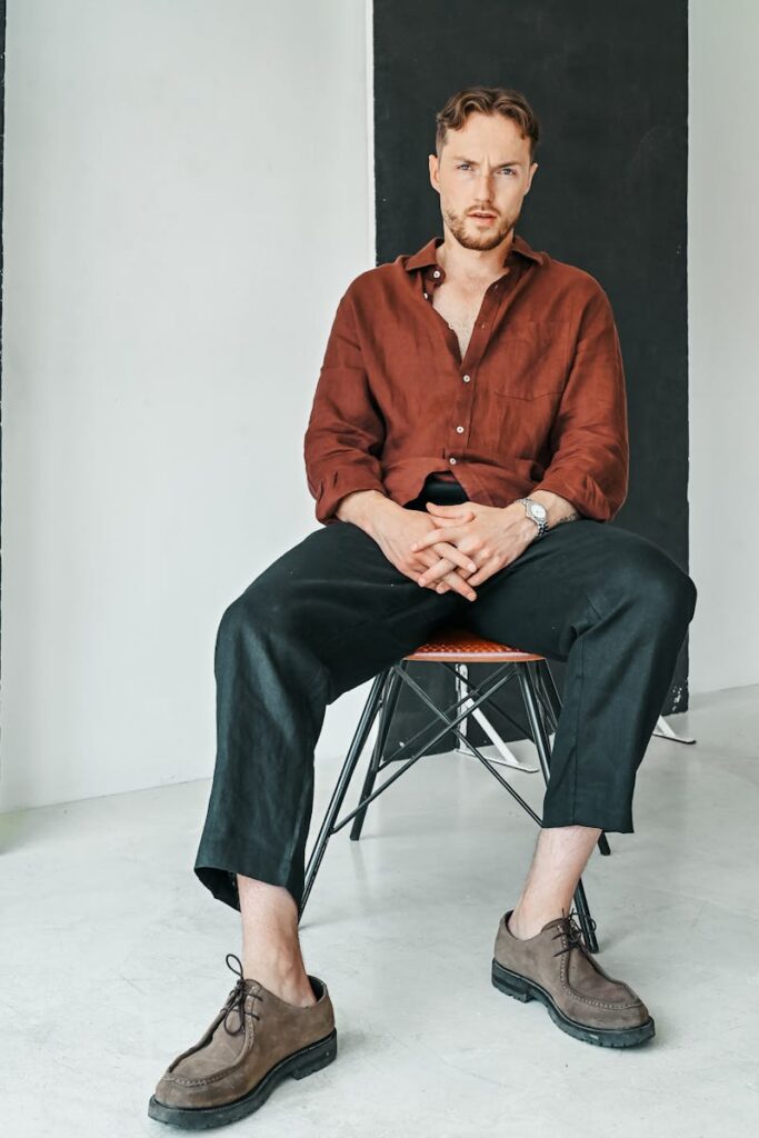 Confident man in casual attire posing on a chair in a contemporary studio.