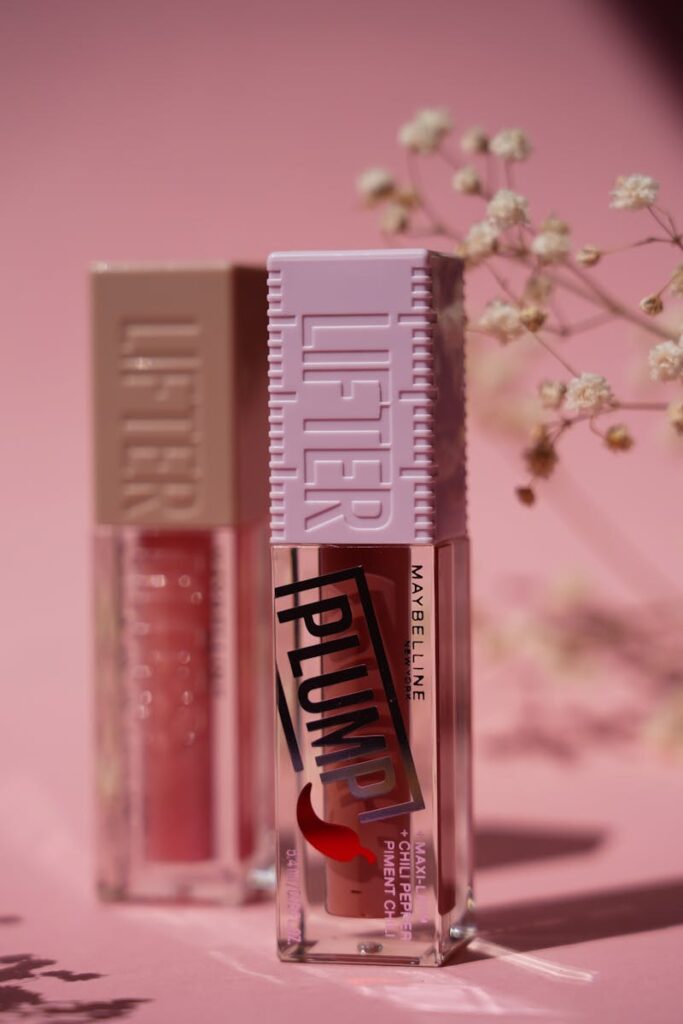 Two shiny lip glosses displayed with delicate flowers on a pink backdrop.