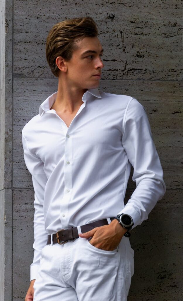 Confident young man in white outfit posing against a concrete wall.