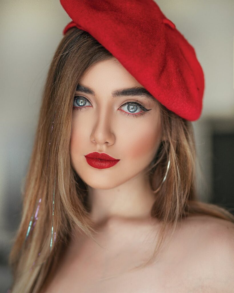 Close-up portrait of a woman with red lips and beret, looking elegantly poised.