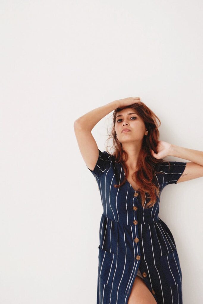 Elegant woman poses in a stylish striped dress against a minimalist background.
