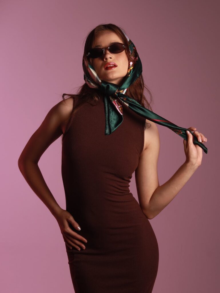 Fashionable woman wearing sunglasses and a headscarf with a confident pose in a studio setting.