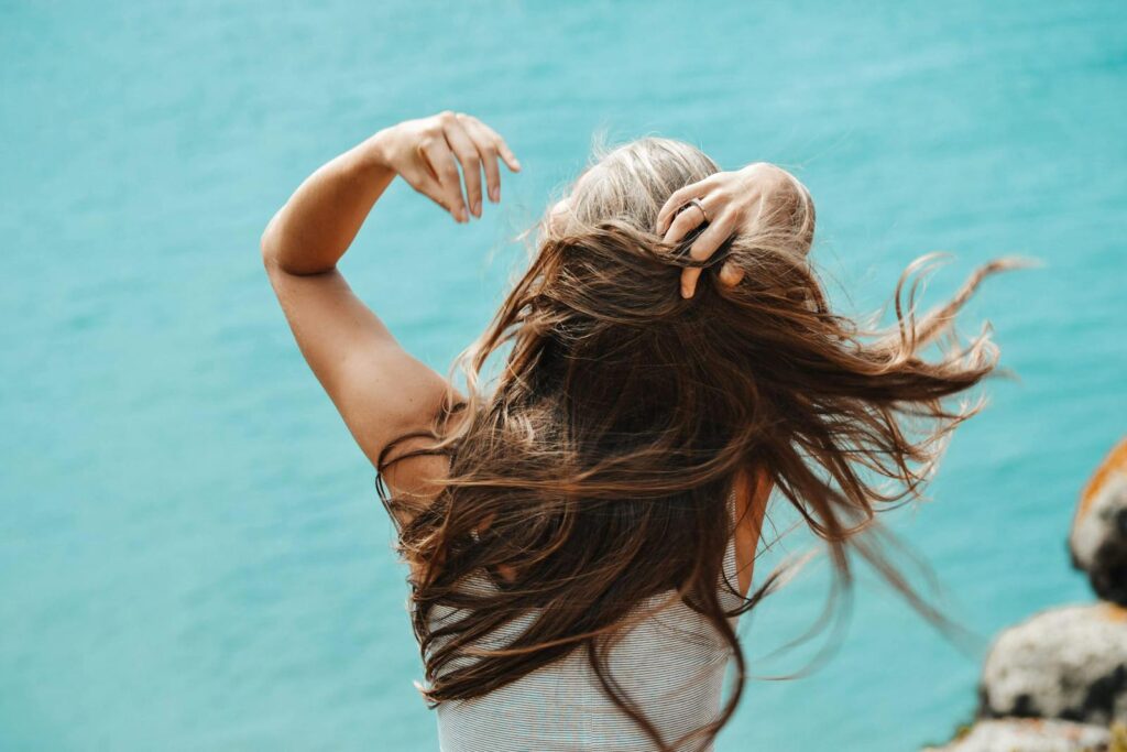 Back view of a woman with flowing hair near the sea in Portugal, capturing a moment of solitude.