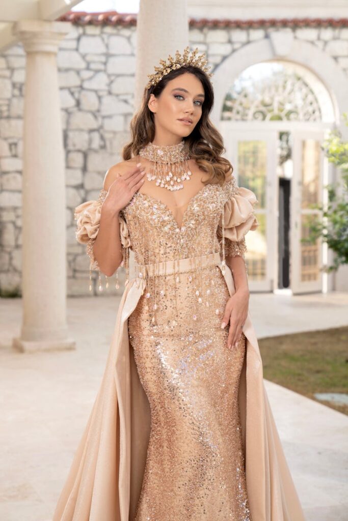 Stunning woman in a shimmering gold gown posing at an elegant courtyard in İzmir.