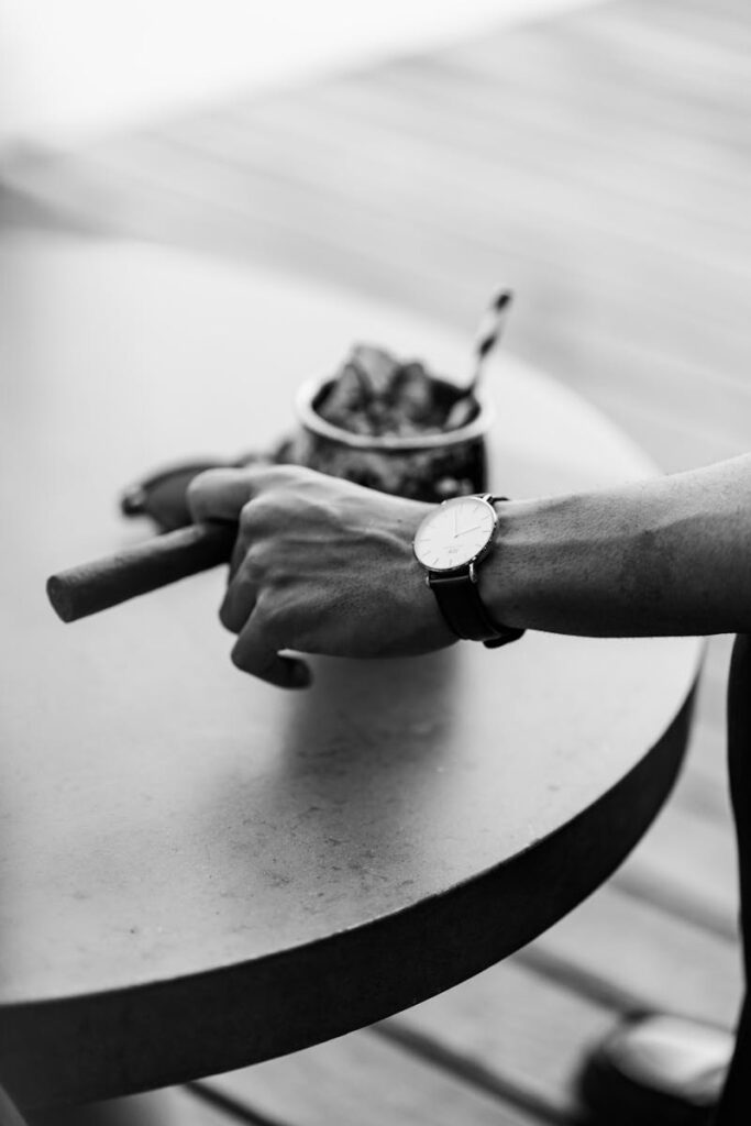 Stylish wristwatch and cigar on a table, captured in classic black and white.