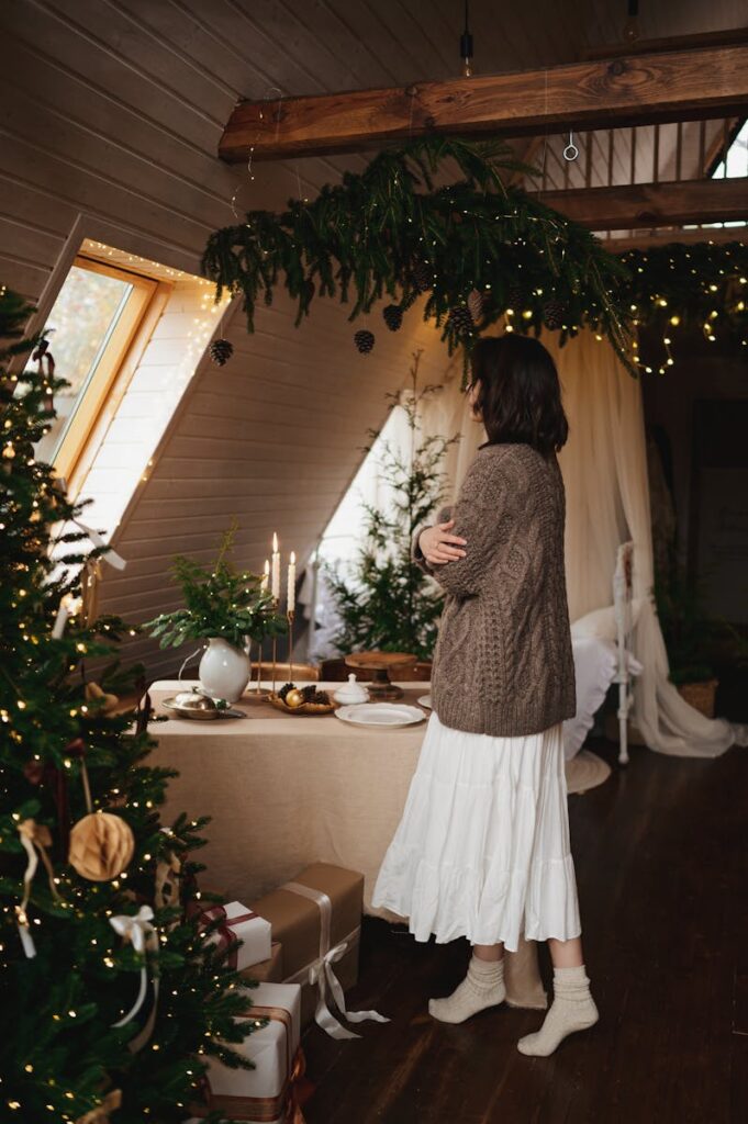 A woman in a cozy attic decorated for holiday festivities with candles and gifts.