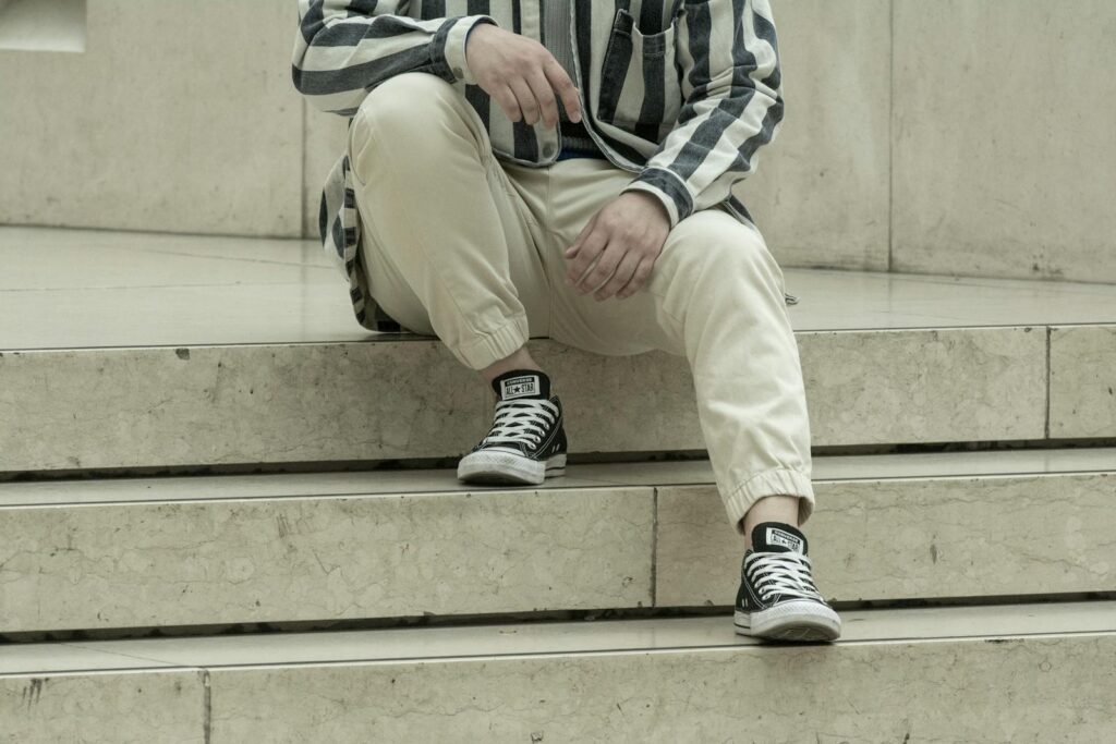 Man in striped shirt and sneakers sits on marble steps, showcasing casual fashion.