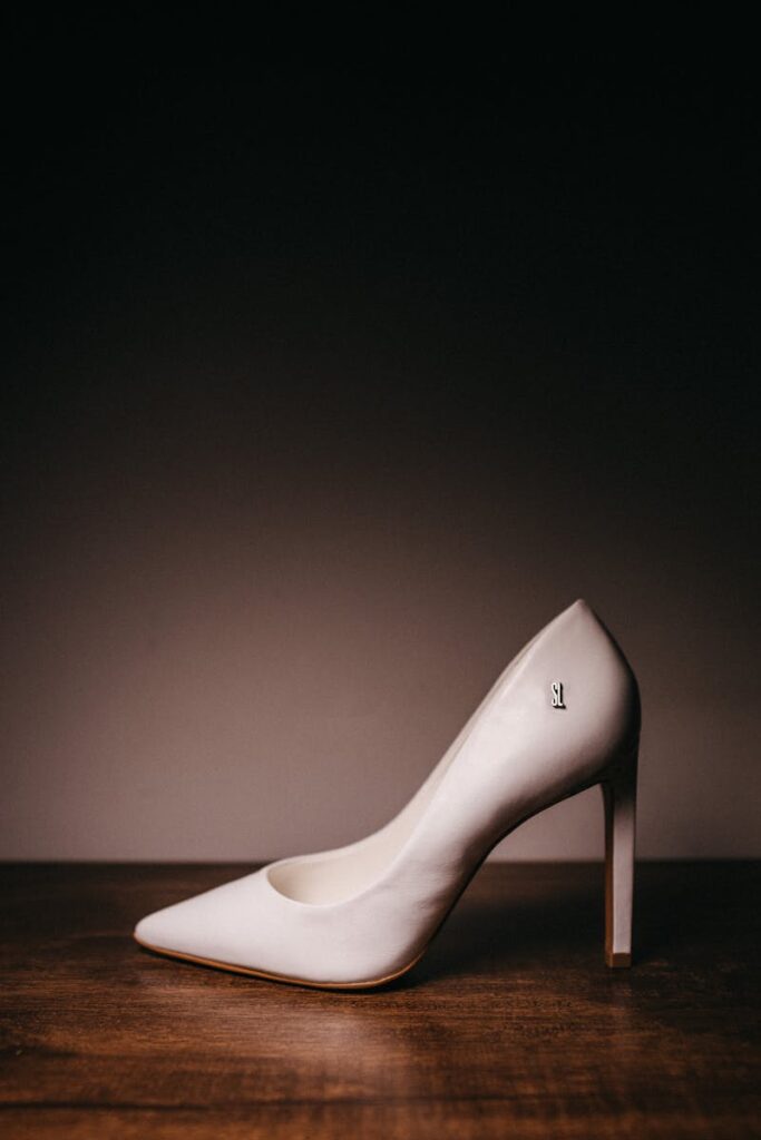Elegant beige high heel shoe showcased on a wooden surface with a dark background, emphasizing modern style.