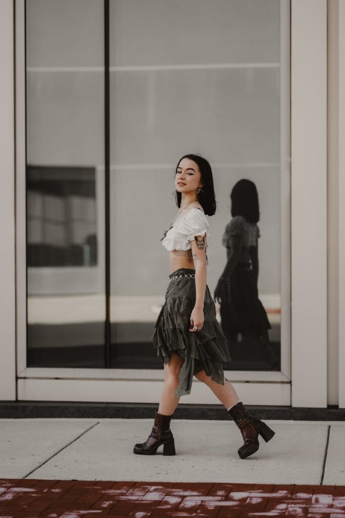 A stylish woman in a trendy outfit walks confidently beside a modern windowed building.