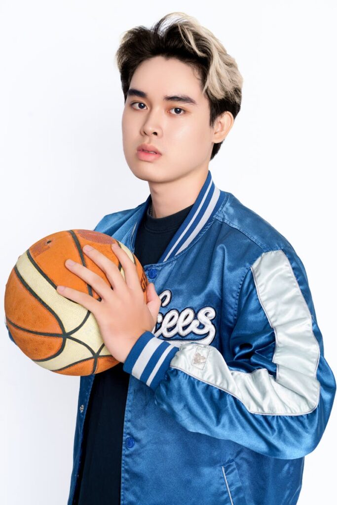 Confident young man in blue bomber jacket holding a basketball, posing in studio.