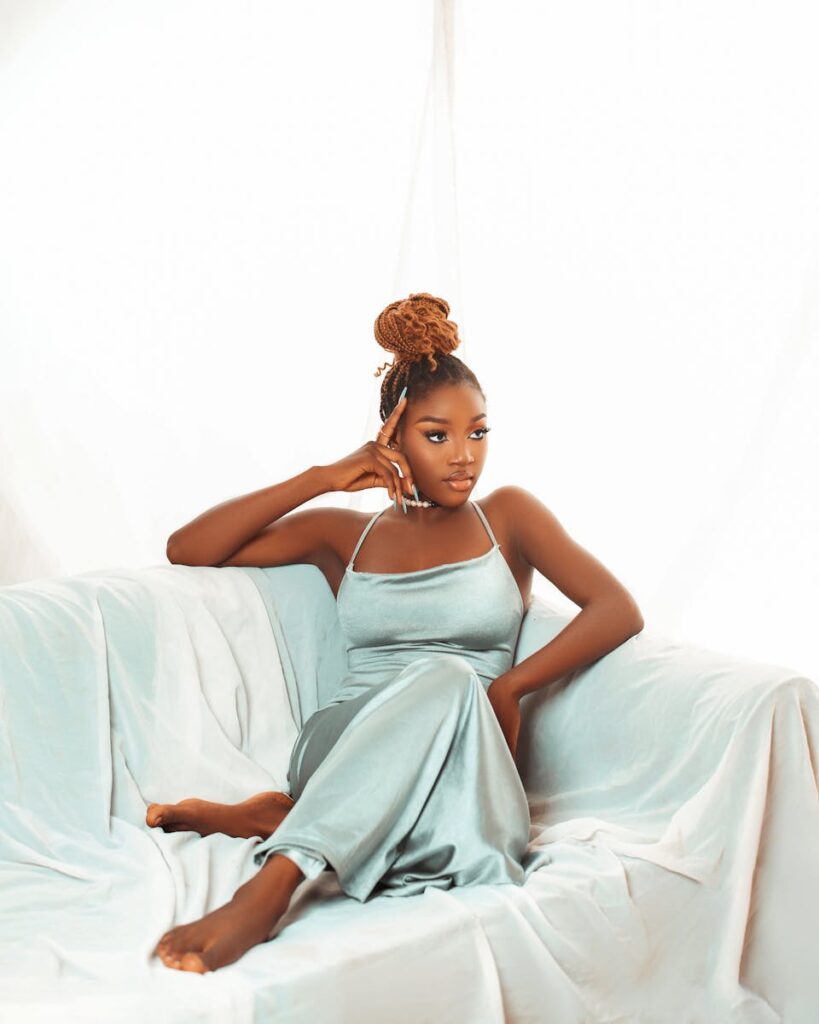 Stylish woman in a silky dress lounging gracefully on a sofa in a serene setting.