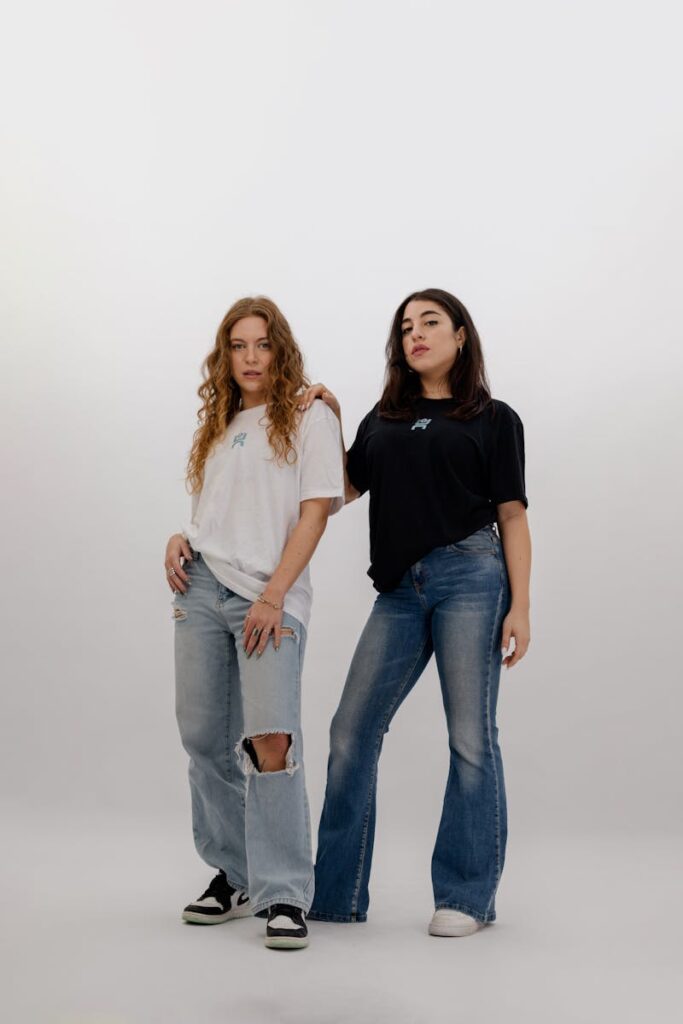 Two women in casual jeans and t-shirts posing confidently in a bright studio.