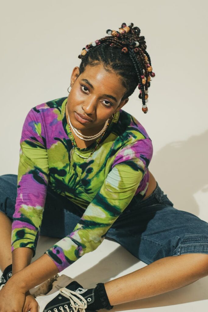Colorful portrait of a woman with beaded hair and tie-dye top sitting casually.