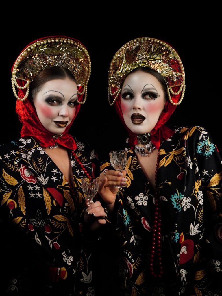 Two women in ornate headdresses and makeup celebrate against a dark backdrop.