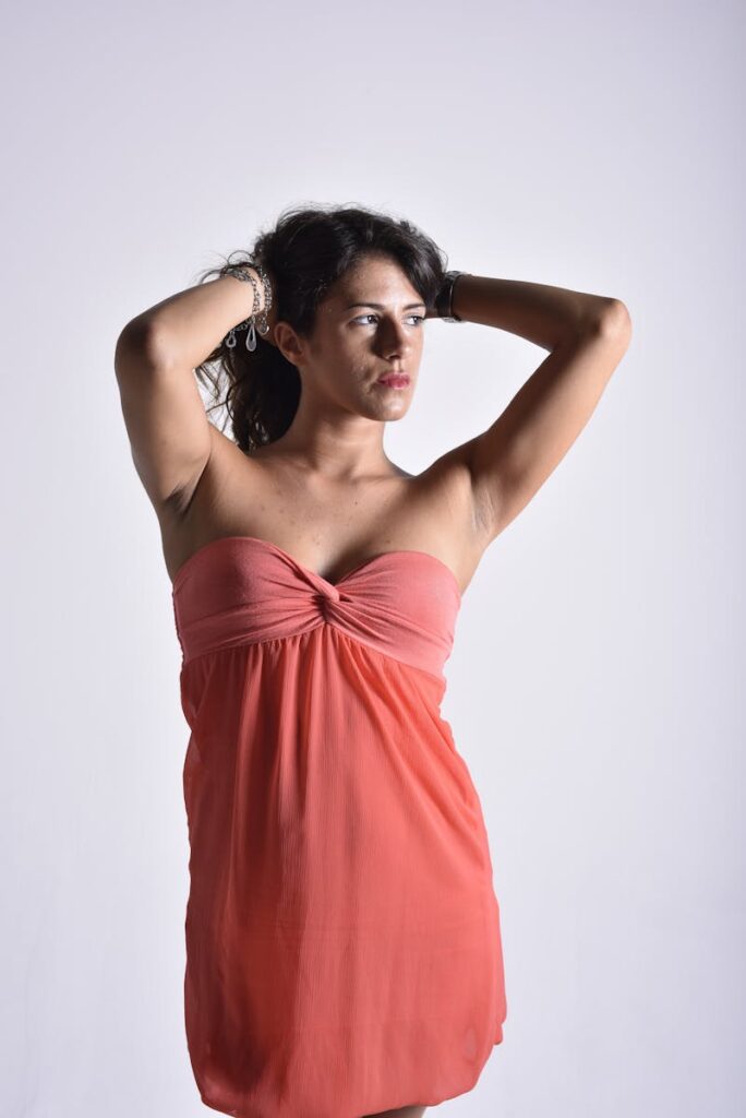 Stunning portrait of a woman in a coral dress posing gracefully against a plain background.