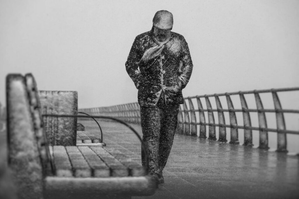 A solitary man walks through a harsh winter storm on a deserted boardwalk.