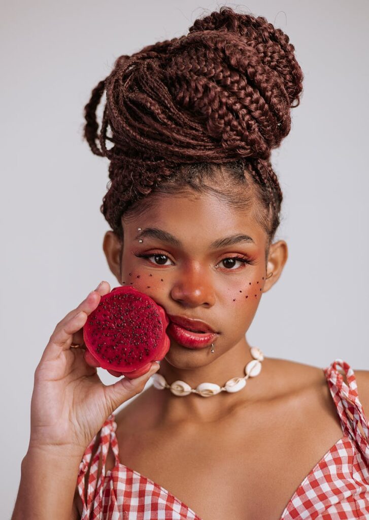 Vibrant portrait of a stylish woman holding a slice of red dragon fruit against a neutral background.
