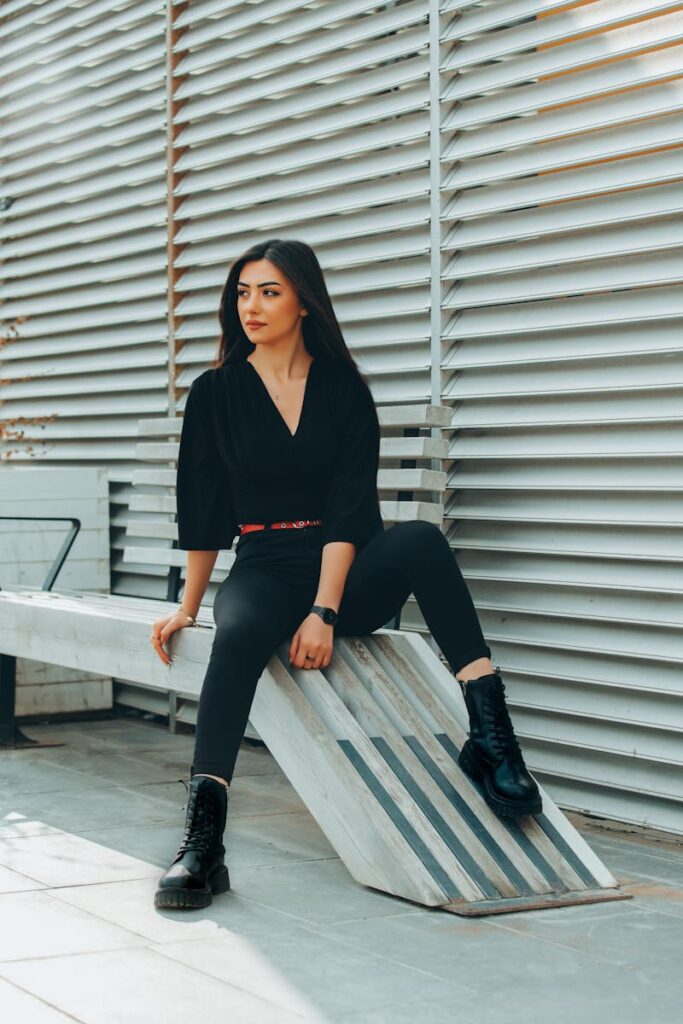 Stylishly dressed woman sitting outdoors in urban setting, conveying modern fashion.