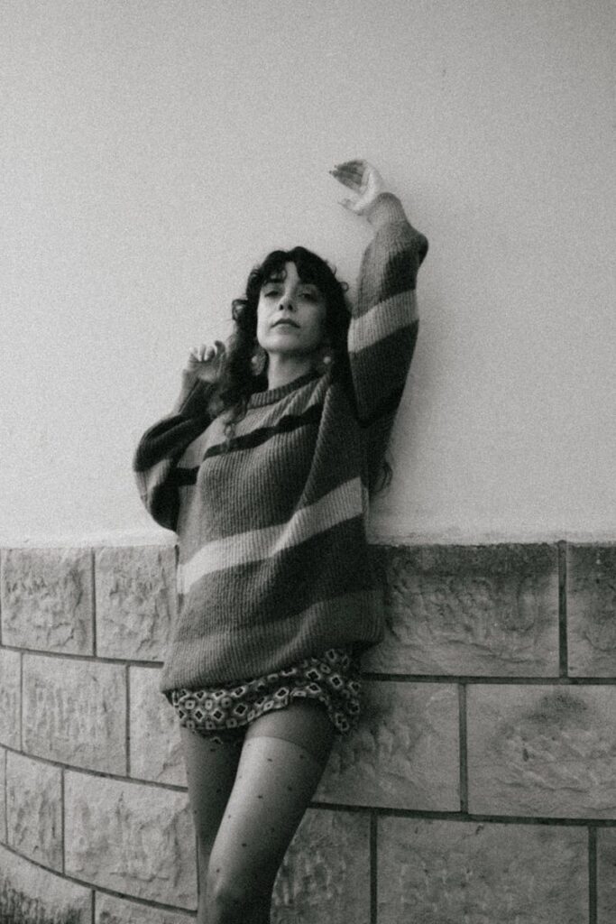 Artistic black and white photo of a young woman leaning against a wall.