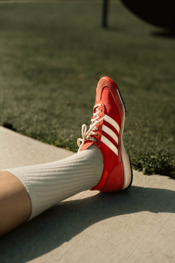 A close-up of a red sneaker with white stripes on pavement, basking in sunlight.