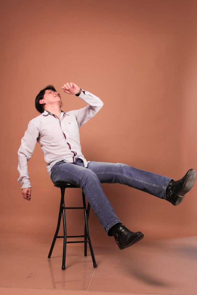 A man in denim jeans and white shirt striking a dynamic pose on a stool in a studio setting.