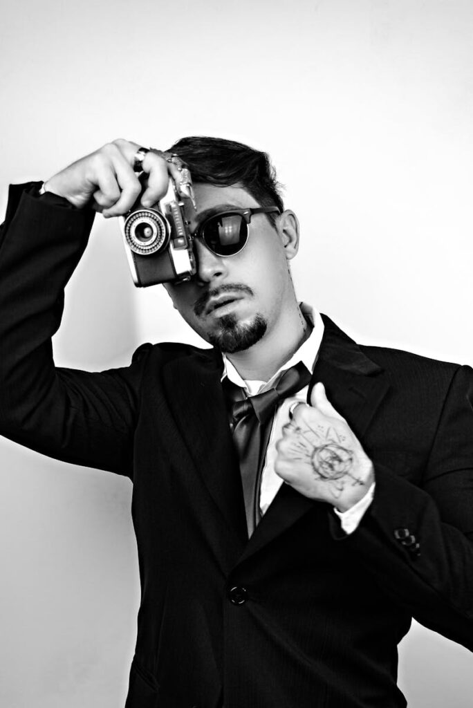 Black and white portrait of a man in a suit posing with a vintage camera.