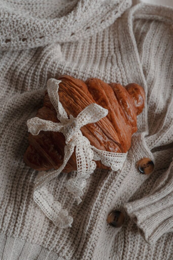 Delightful croissant wrapped in lace on a soft knitted sweater, evoking cozy winter vibes.