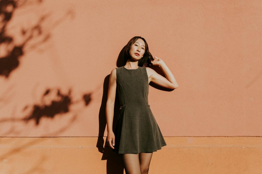 Stylish woman in fashionable dress standing beside a warm-colored wall showing shadows.