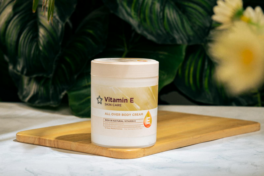 Vitamin E skincare cream on wooden tray with botanical background.