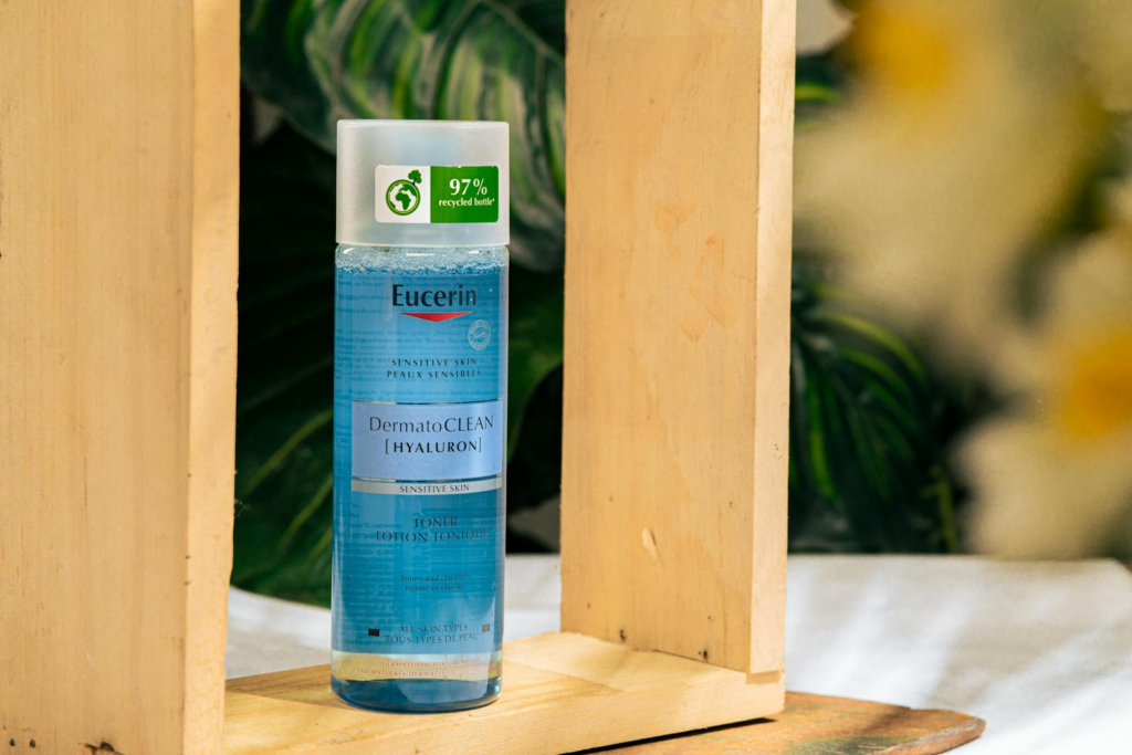 Eucerin DermatoCLEAN Hyaluron toner bottle surrounded by wooden frame and plants.