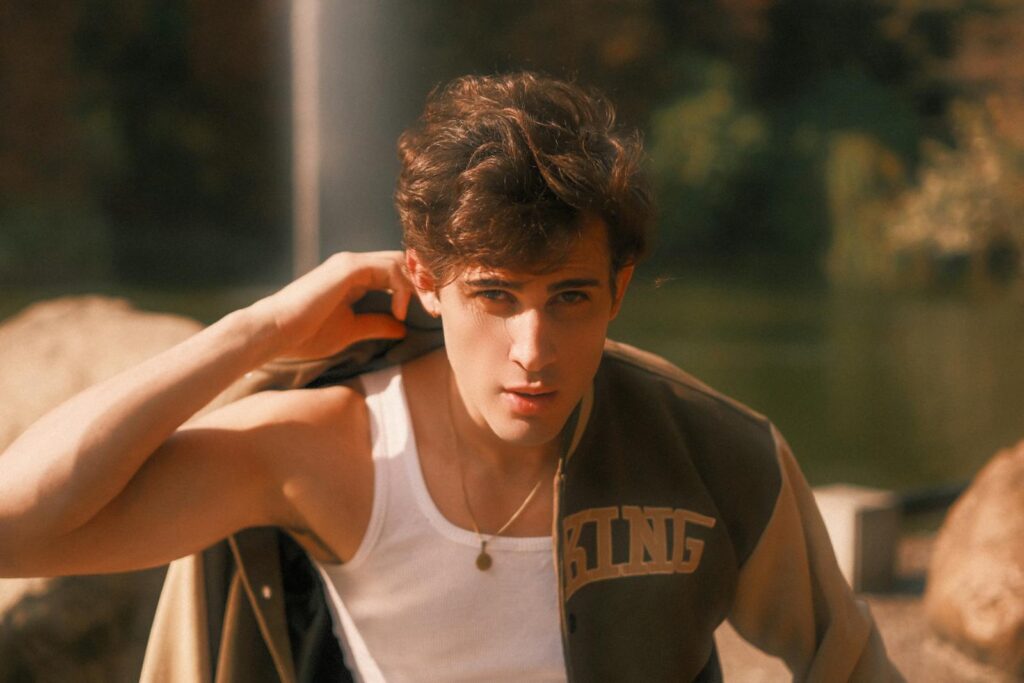A young adult male poses thoughtfully by a lake, soaking in the warm autumn sun.