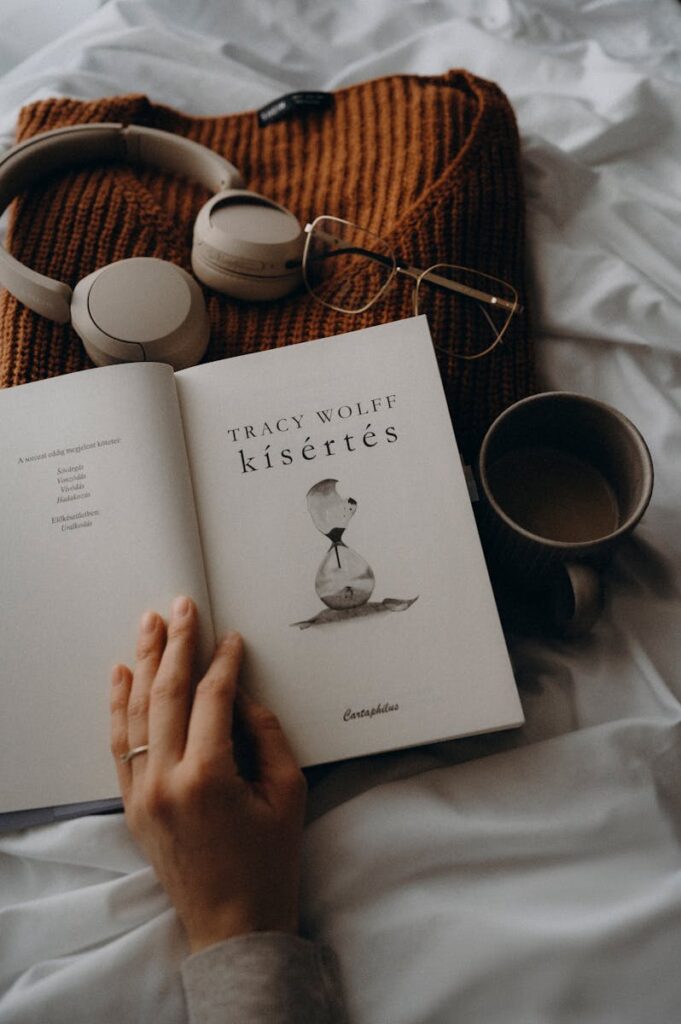 A cozy setup with a book, headphones, glasses, and a coffee cup on a bed. Perfect for relaxing moments.