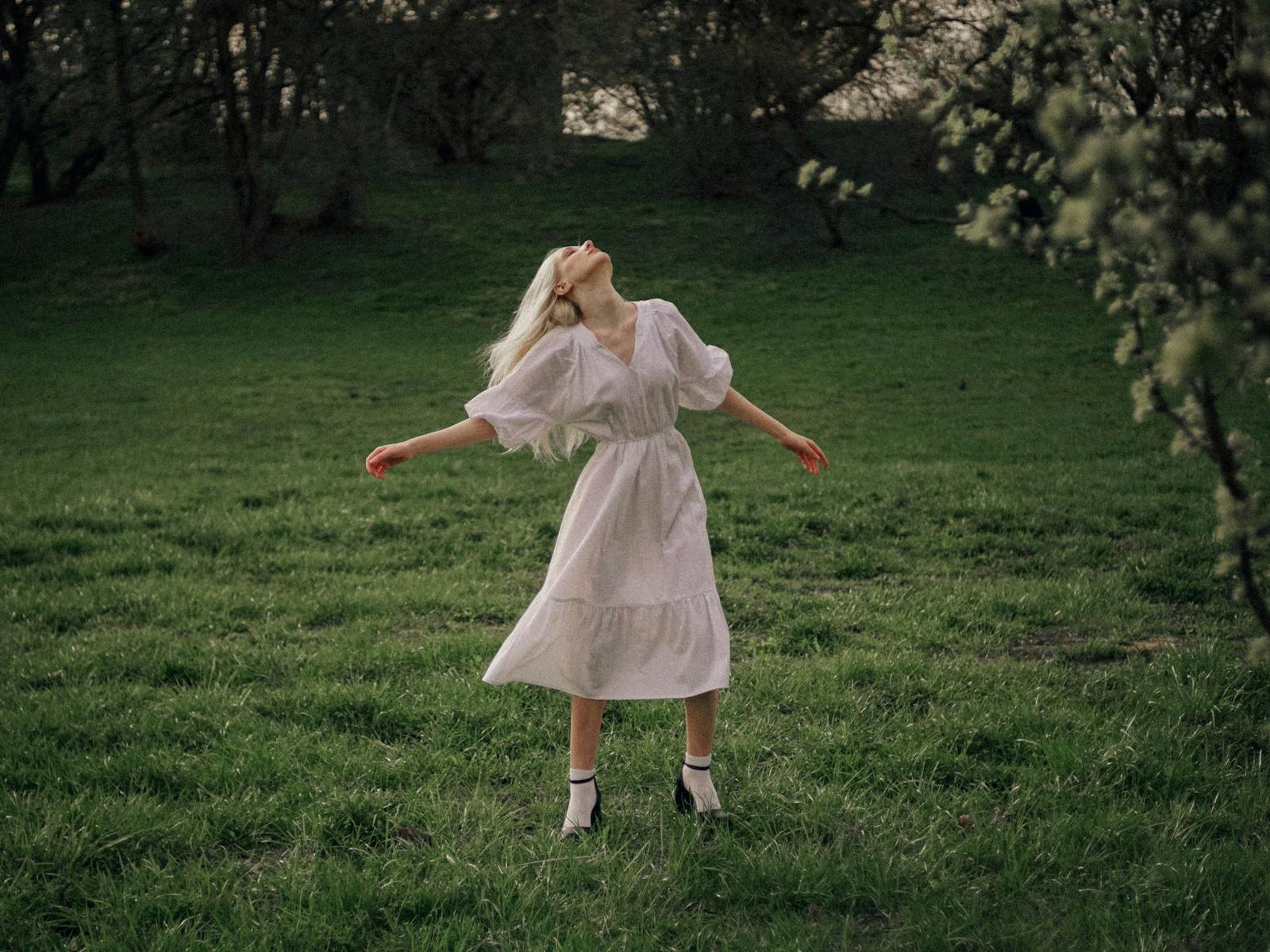 A young woman in a white dress enjoying a serene moment outdoors among lush greenery.