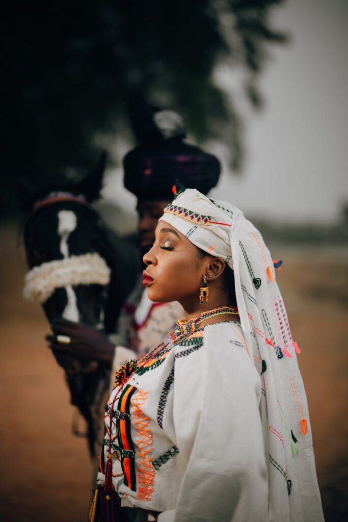 Woman in colorful African traditional dress poses with a horse outdoors.