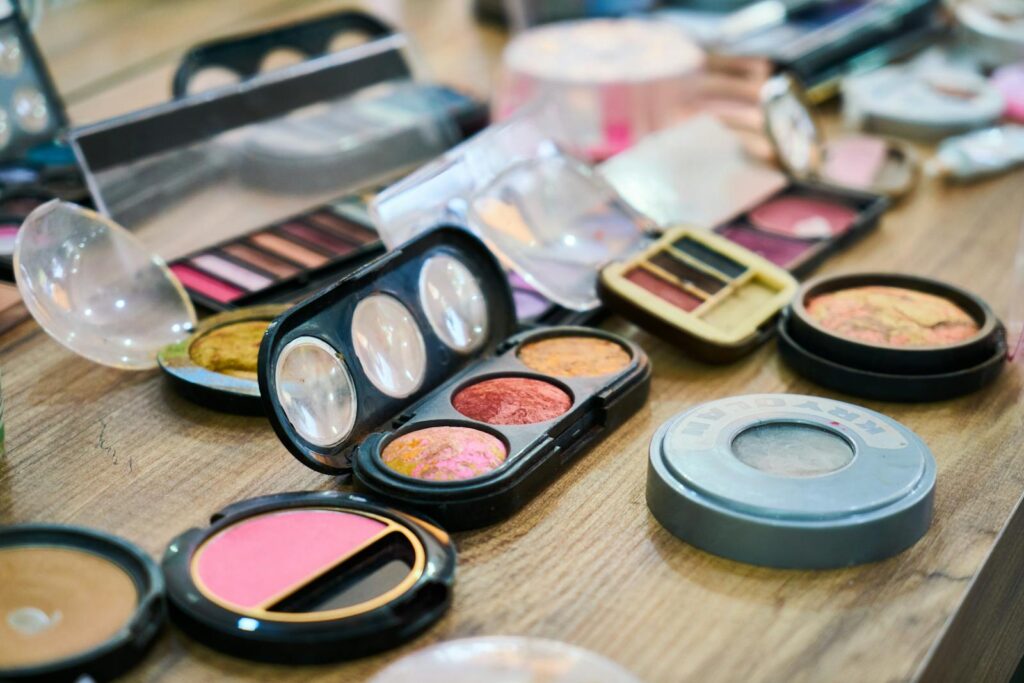 A variety of colorful makeup palettes and cosmetics organized on a wooden table.