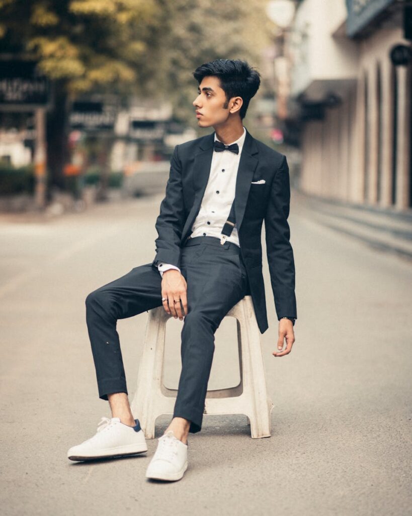 A stylish man in a tuxedo sitting street-side against an urban backdrop.