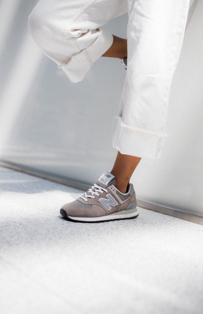 Close-up of a woman's casual outfit featuring grey sneakers and rolled-up white jeans in a bright setting.