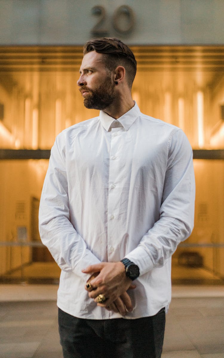 Bearded man in white shirt posing pensively outdoors in an urban setting.