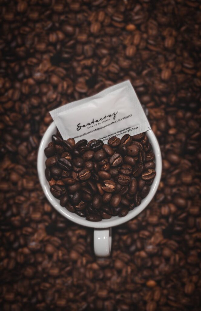 Coffee beans in a cup with focus on a packet, surrounded by coffee beans.
