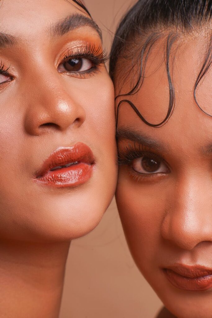 Intimate close-up of two women with striking eye makeup and lipstick.