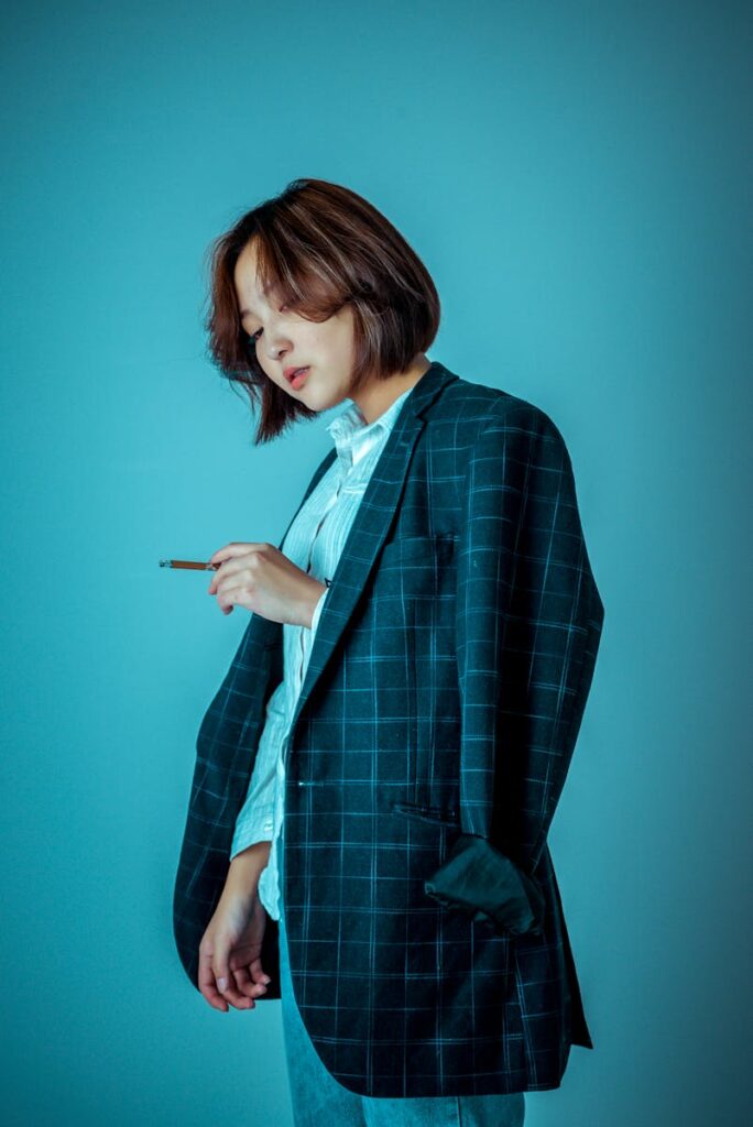 A fashionable woman in a plaid suit smokes indoors, exuding style and confidence.